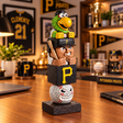 A Pittsburgh Pirates-themed wooden stacking figurine displayed on a wooden table in a themed room. The figurine features a green bird character on top, followed by a wooden figure wearing a black cap with a yellow 'P' logo, a black box with a large yellow 'P', and a white baseball with a painted face at the bottom, all resting on a dark wooden base.